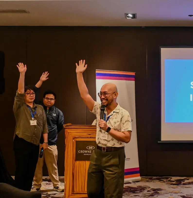Three presenters raise their hands at a podium in a Crowne Manila conference room, beside a projection slide that reads "CITIZEN SATISFACTION INDEX SYSTEM (CSIS)".