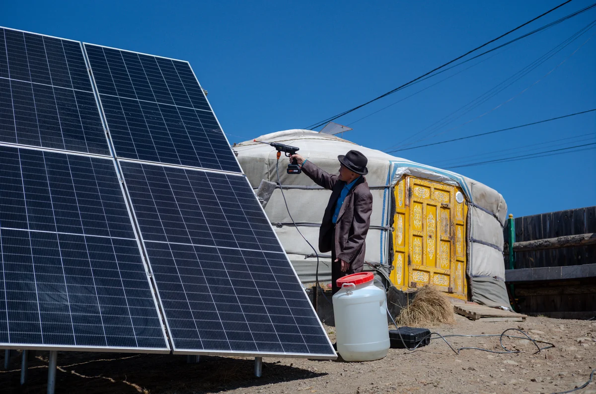 A man cleans solar panels outside his ger, maintaining clean energy in a remote Mongolian homestead.