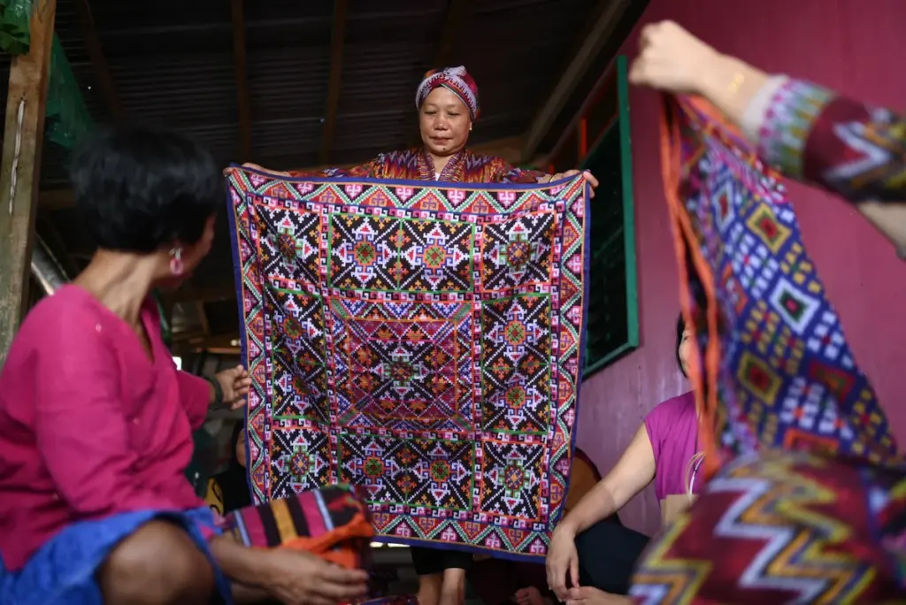 A Bangsamoro woman entrepreneur displays a richly patterned handwoven textile to a group of women during a local business skills initiative.