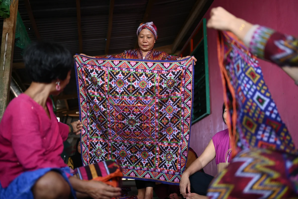 A Bangsamoro woman entrepreneur displays a richly patterned handwoven textile to a group of women during a local business skills initiative.